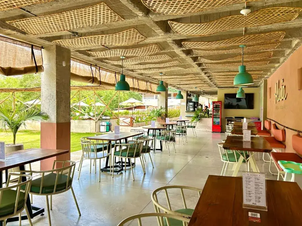 Comedor de Alaia con techo de esterilla, mesas de madera y jardín alrededor