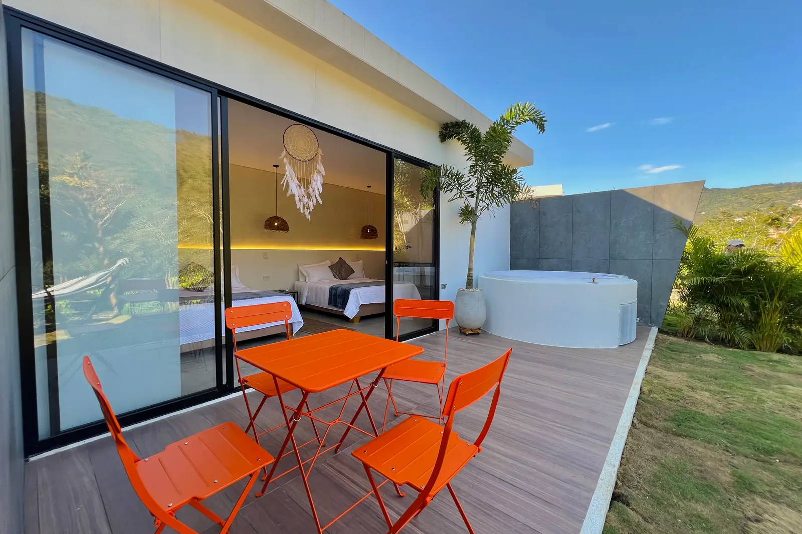 Terraza de la cabaña familiar con mesa y sillas naranjas, jacuzzi y montaña bajo el cielo azul