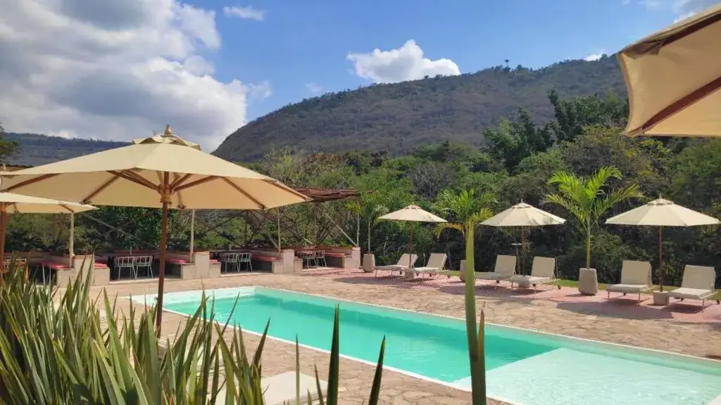 Piscina azul con parasoles y la montaña cubierta de bosque detrás